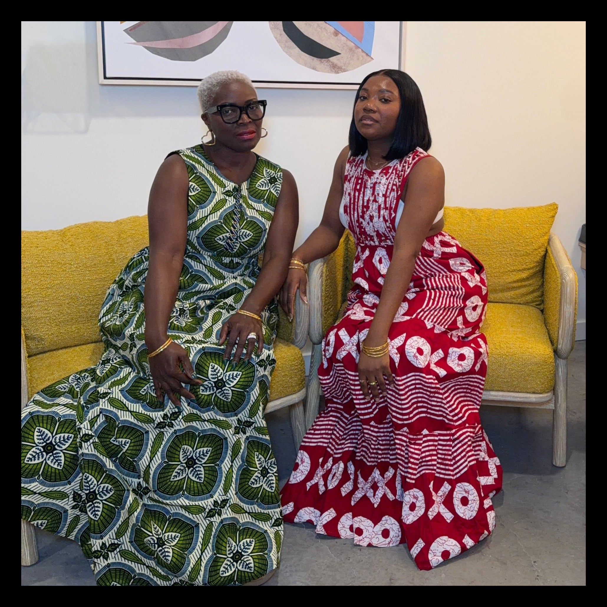 Two women sitting on a yellow couch in a room with a colorful abstract painting on the wall.